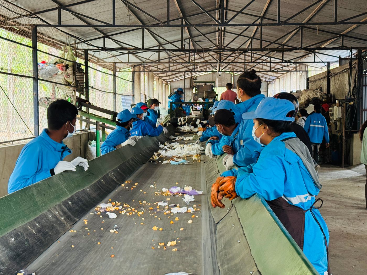 Equipe uniformizada separando materiais recicláveis em esteira de triagem